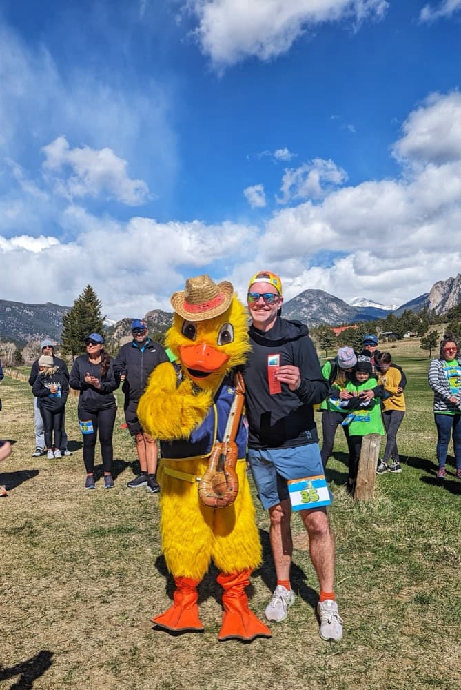 Blake at a 5K race in Estes Park, posing with a giant duck mascot